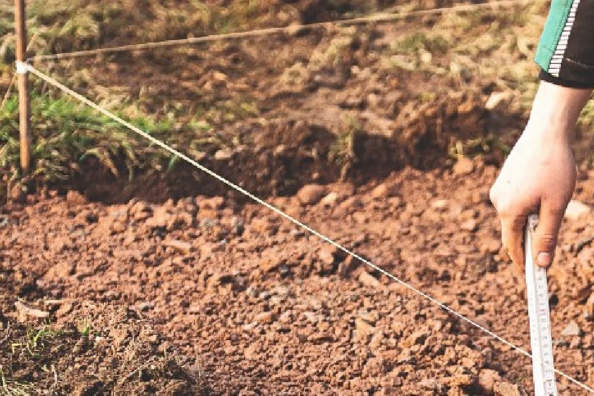 Person misst mit Zollstock Erde ab